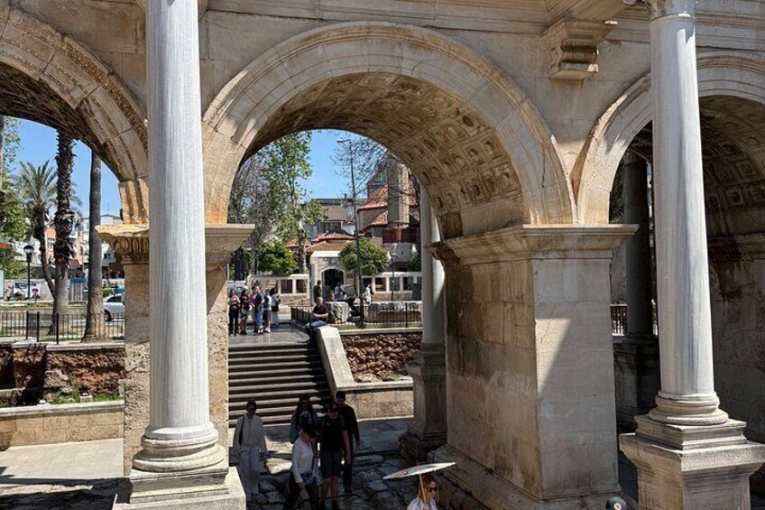 Un arc en pierre antique, flanqué de colonnes, un escalier et des personnes qui se promènent. 2