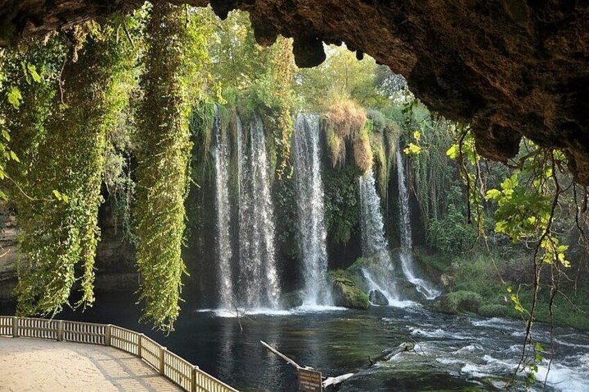 A waterfall cascading into a river, surrounded by lush greenery and a wooden walkway. 1
