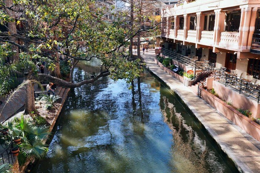 Ein Kanal mit einem überhängenden Baum, ein Gebäude mit Balkonen und ein Fußweg. 3