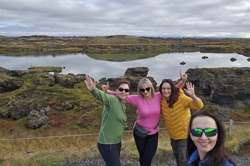 Three people standing by a lake with rocky terrain and a cloudy sky. 3