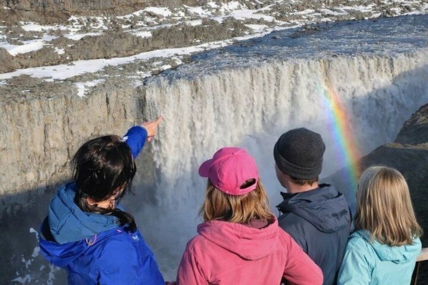 A group of people observing a waterfall with a rainbow. 2