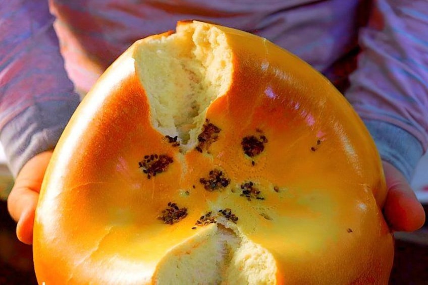 A person holding a large, round, orange-colored bread with a bite taken out of it. 2
