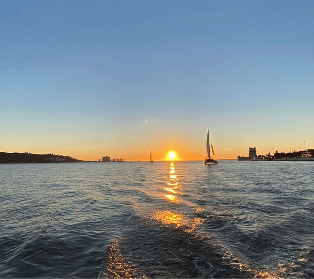 A sunset over a calm sea with a sailboat and distant buildings. 5