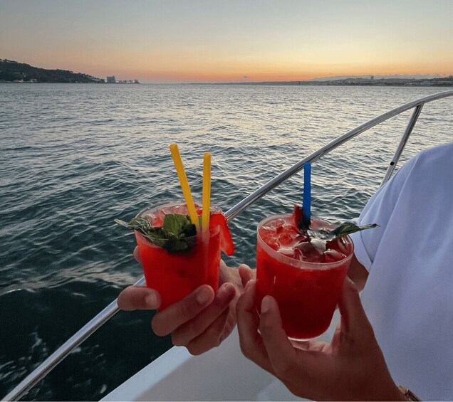 Two people holding red drinks with straws and mint leaves on a boat. 3