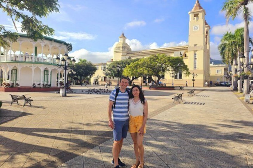 A man and woman standing in a plaza with a clock tower and a building with a dome in the background. 5