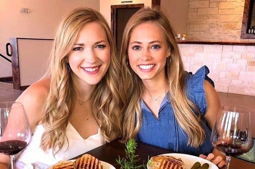 Two people sitting at a table with food and wine. 2