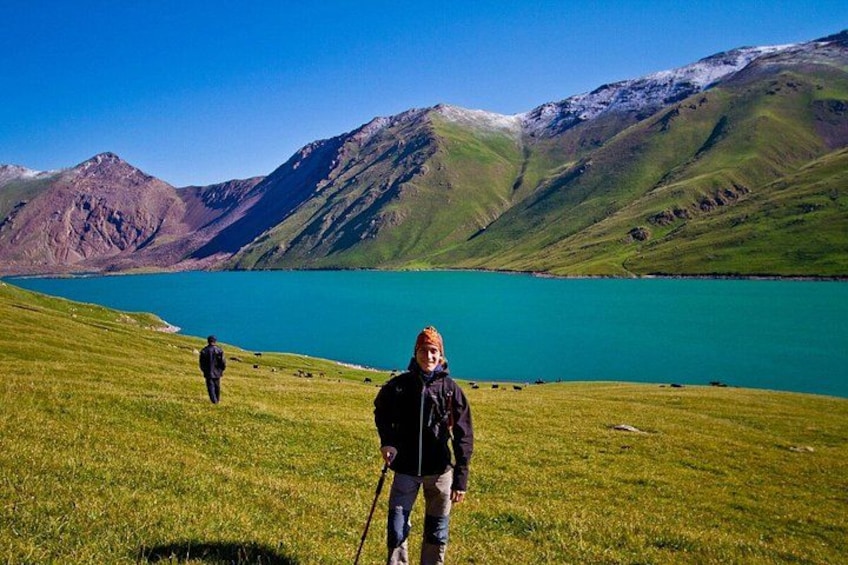 Una persona caminando sobre una colina con hierba, un lago y montañas al fondo. 5