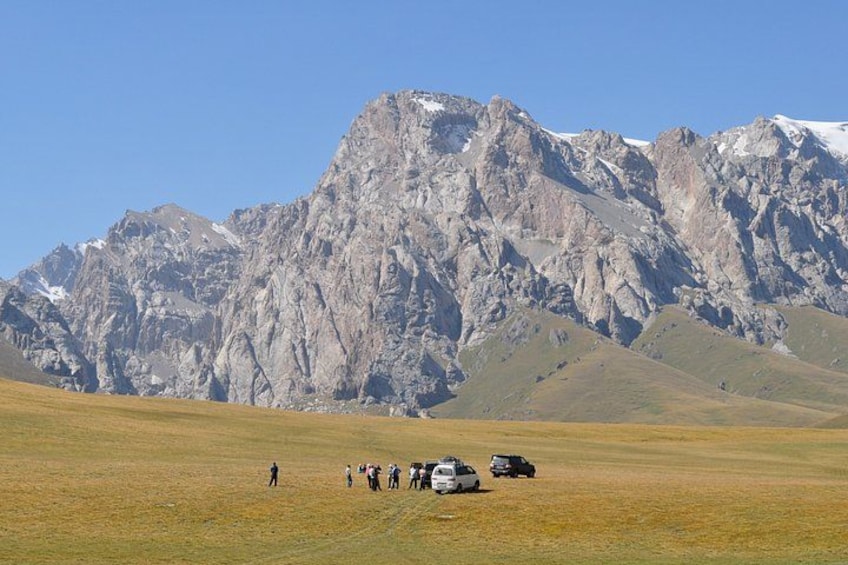 Paisaje montañoso con un grupo de personas y vehículos en un campo. 3