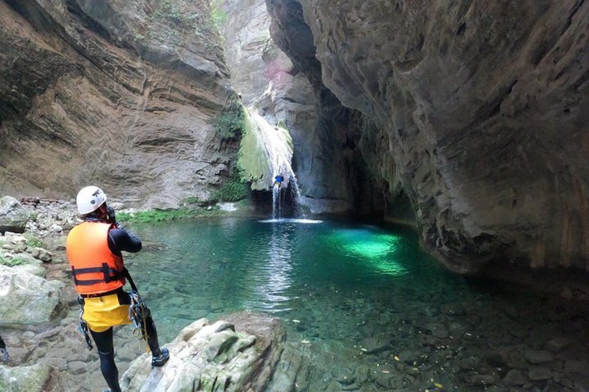 A person in a helmet and life jacket observing a waterfall in a rocky canyon. 5