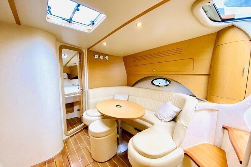 Een compact, goed verlicht interieur met een ronde tafel, zachte zitplaatsen en een klein raam. 4
