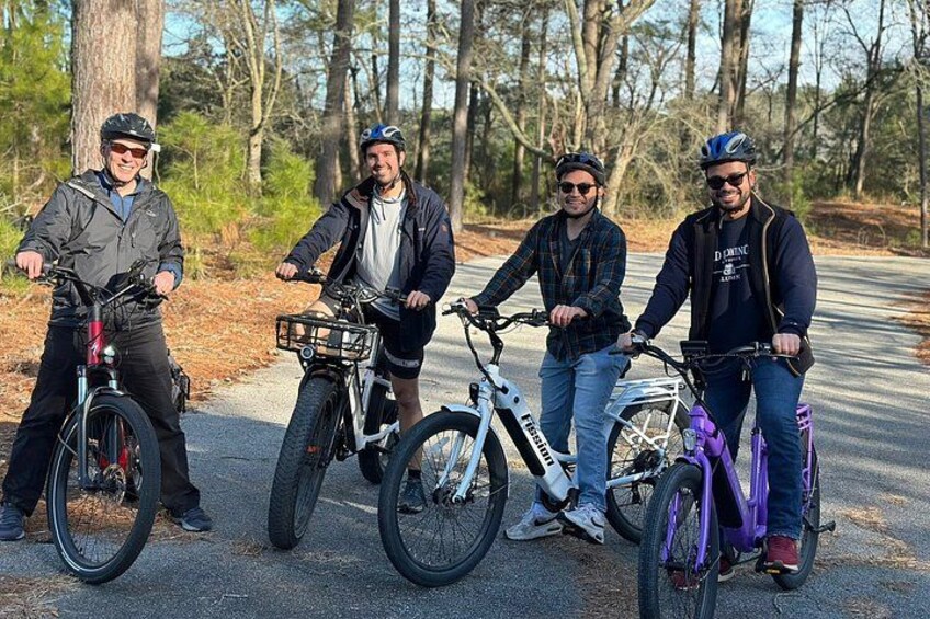 Four people on bicycles on a paved path surrounded by trees. 5