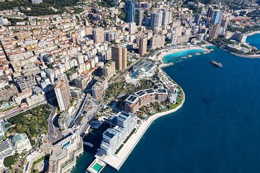 An aerial view of a coastal city with dense urban development, a marina, and a curved coastline. 1