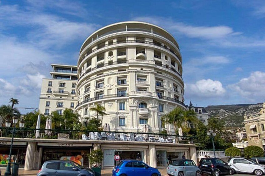 A multi-story building with balconies, surrounded by parked cars and palm trees. 3