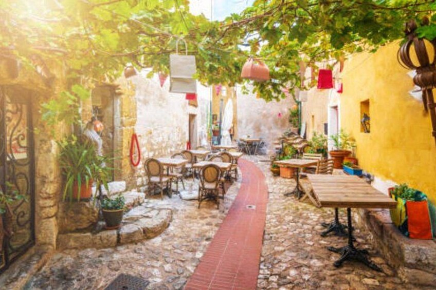 A cobblestone street with outdoor seating, potted plants, and hanging decorations. 4