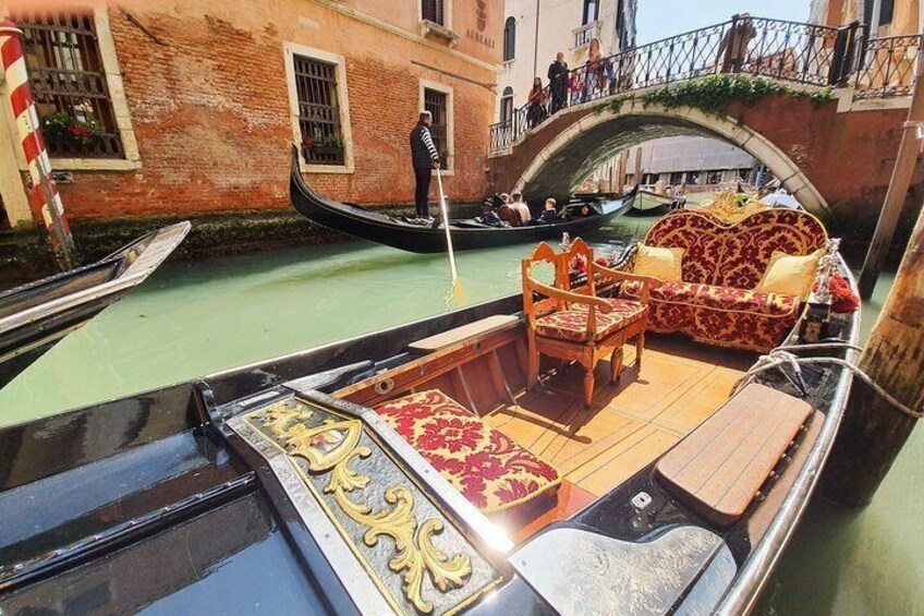 A gondola with ornate furniture and a bridge in the background. 1