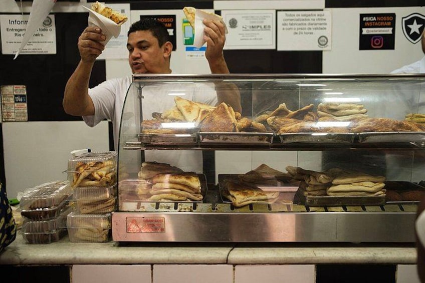 En person serverer mad fra en disk med forskellige sandwiches og kager i en glasmontre. 4