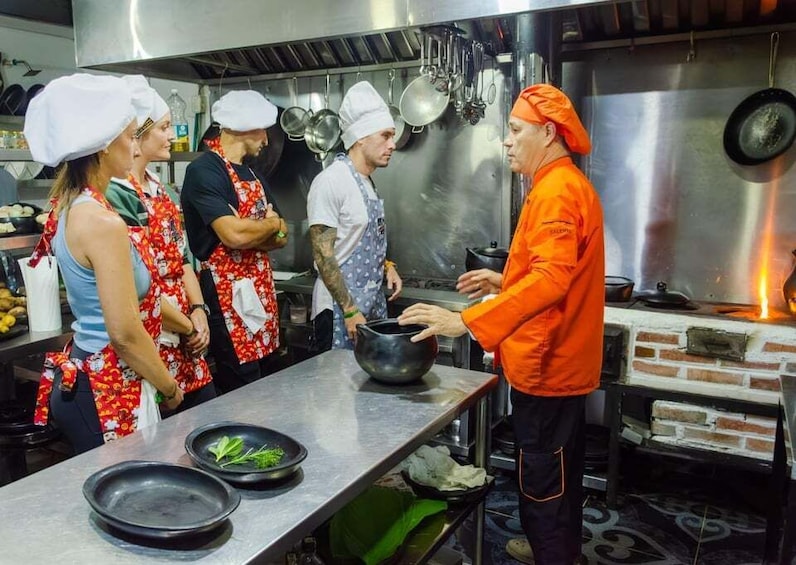 A kitchen with chefs in aprons, a large pot, and a brick oven. 3
