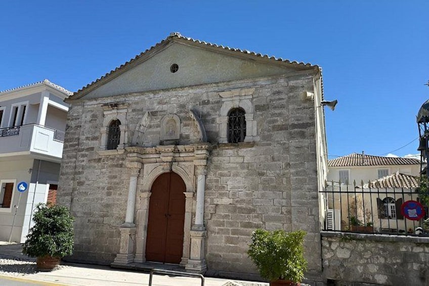 A stone building with a brown door and arched windows, surrounded by potted plants and a clear blue sky. 3