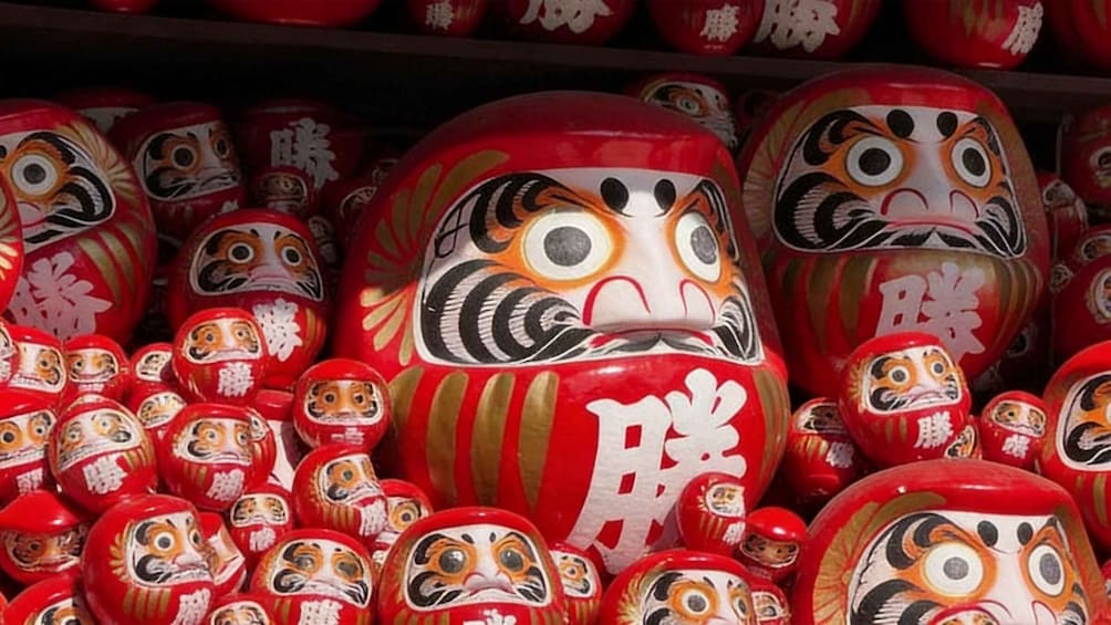 A collection of red and white painted Japanese dolls, some with tiger faces, displayed on shelves. 4