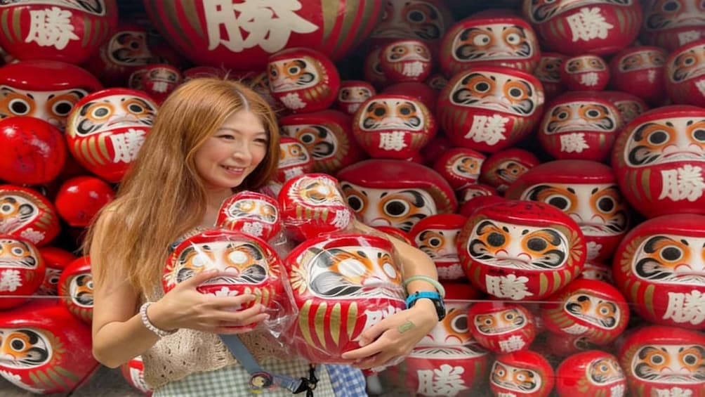 A person holding a red and white painted doll with a tiger face, surrounded by similar dolls in a store. 1