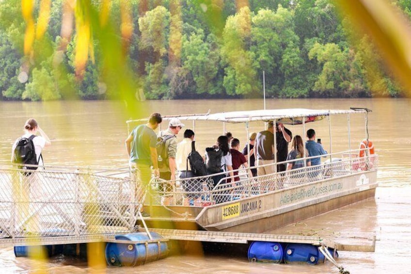A riverboat with passengers, docked at a pier with a forested riverbank in the background. 4