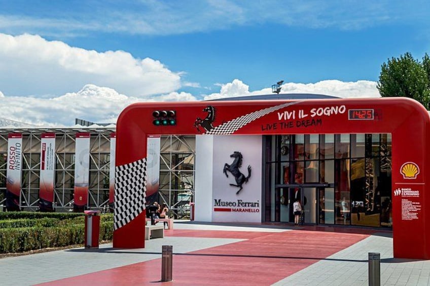 Une arche rouge ornée du logo Ferrari et des inscriptions « Museo Ferrari Maranello » et « Vivi il sogno ». 1