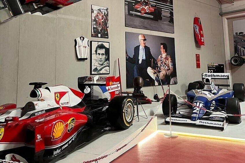Un garage pour voitures de course abritant deux voitures de compétition, une Ferrari rouge et une McLaren bleue, ainsi qu’un podium avec un trophée. 3