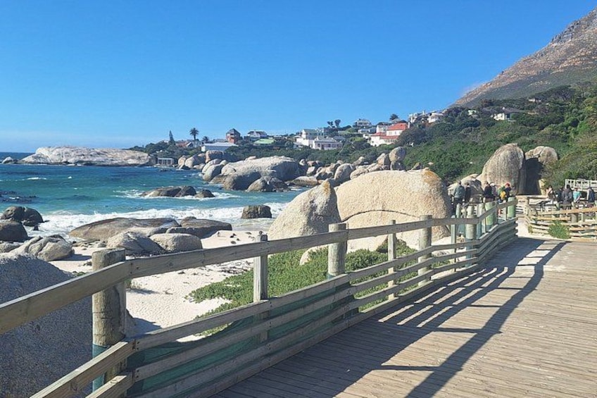 A wooden boardwalk with large boulders, a beach, and houses in the background. 5