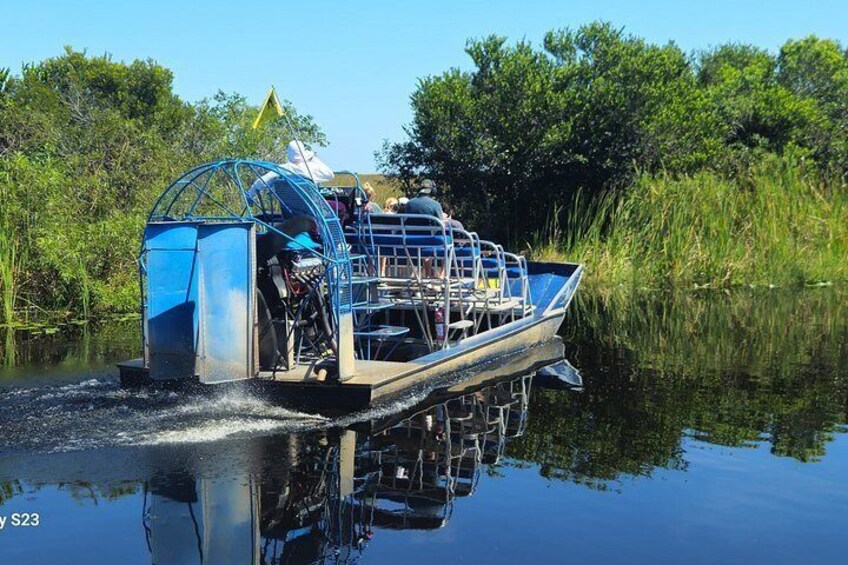 A houseboat with a blue canopy, moving through a calm river surrounded by greenery. 4