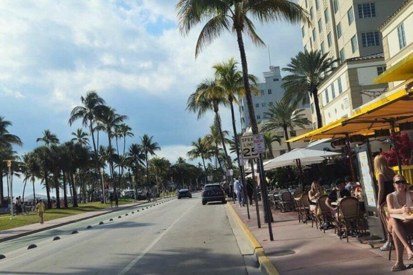 A street lined with palm trees, outdoor cafes, and a clear sky. 1