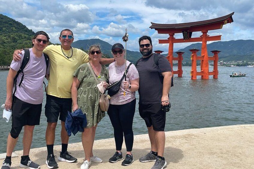 En gruppe mennesker står ved vandet med en rød torii-port i baggrunden. 2