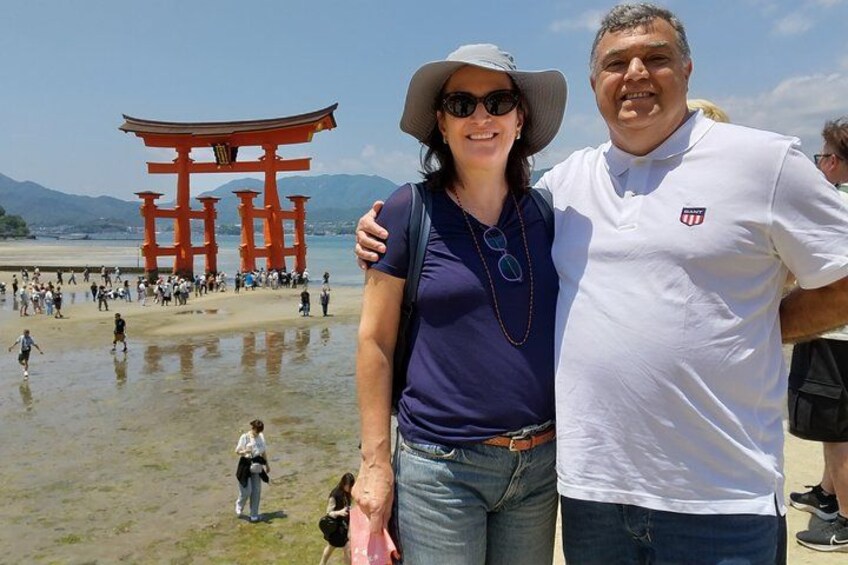 Una pareja parada frente a un torii rojo, con una playa y montañas al fondo. 5