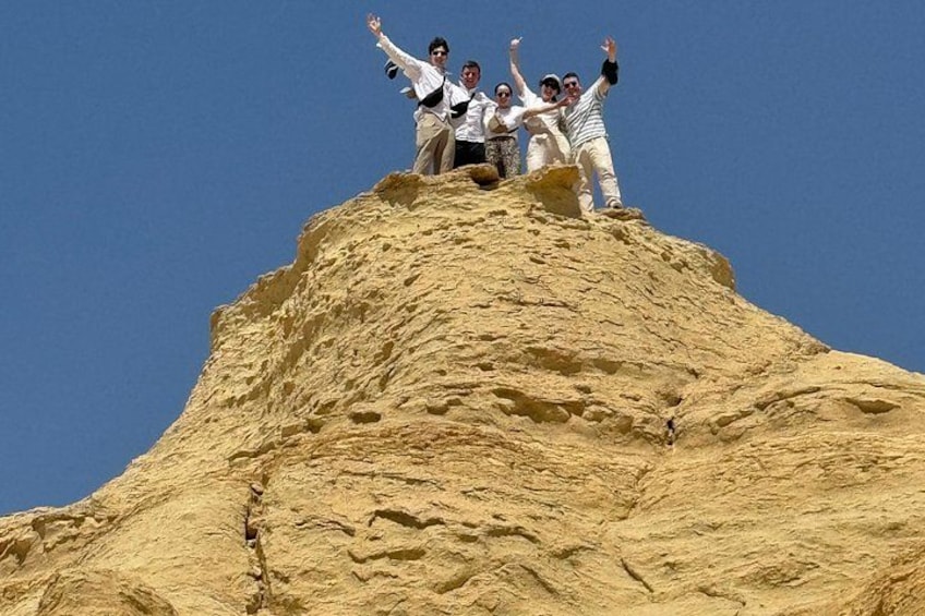 Eine Gruppe von Personen steht auf einem sandigen Hügel und streckt die Arme in die Höhe. 3