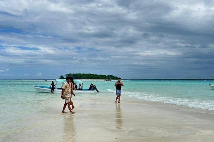 Ein Strand mit Spaziergängern, Booten im Wasser und einer entfernten Insel. 1