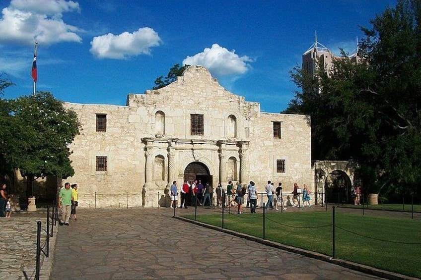 A historic stone building with a large archway, surrounded by a paved walkway and a grassy area. 3