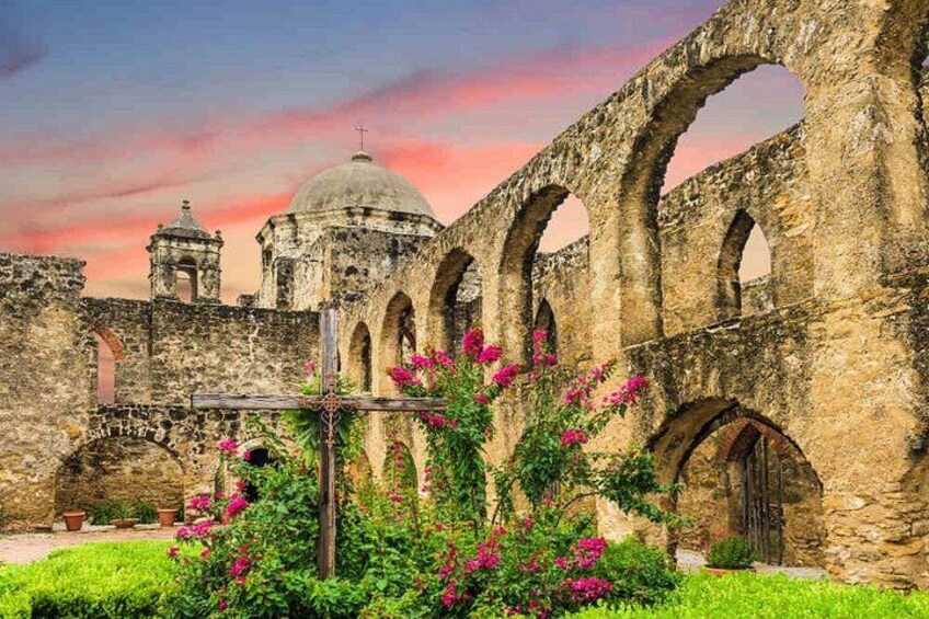 An ancient stone structure with arches and domes, surrounded by lush greenery and flowering plants. 2