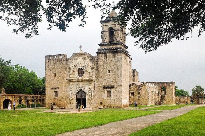 An old stone building with a bell tower, surrounded by a grassy area and trees. 4