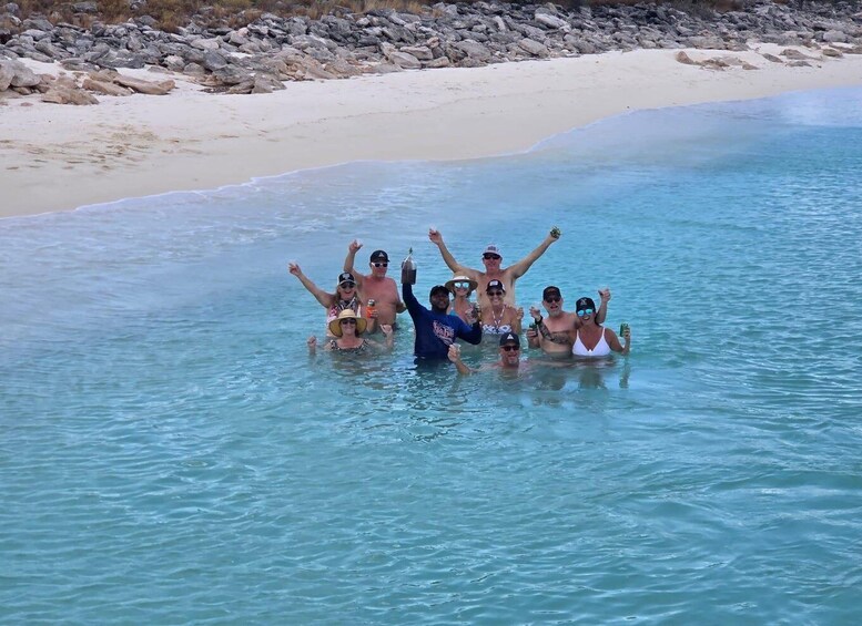 A group of people in clear blue water on a sandy beach with rocks in the background. 4