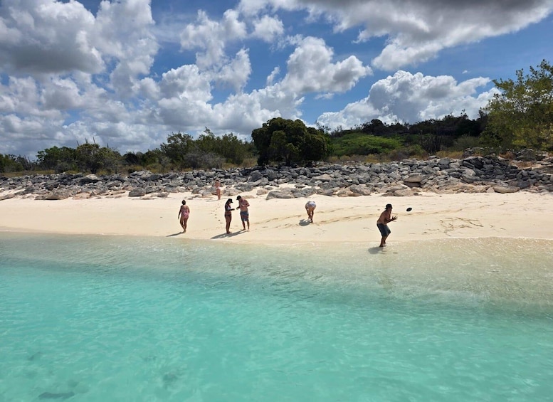 A beach with clear turquoise water, people walking on the sand, and a rocky shoreline with vegetation. 3