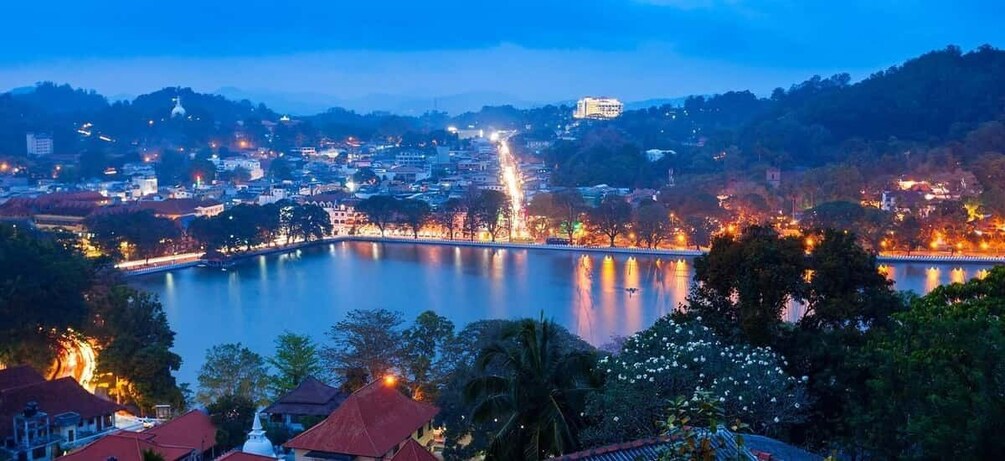 A cityscape at dusk with a lake, illuminated buildings, and a prominent hilltop structure. 5