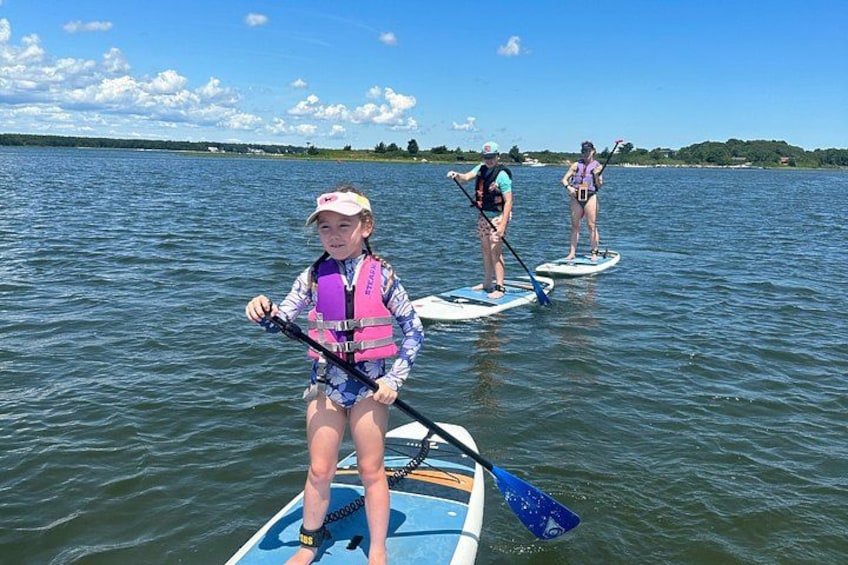 Drie mensen staan op paddleboards op een kalm meer, onder een heldere lucht. 3