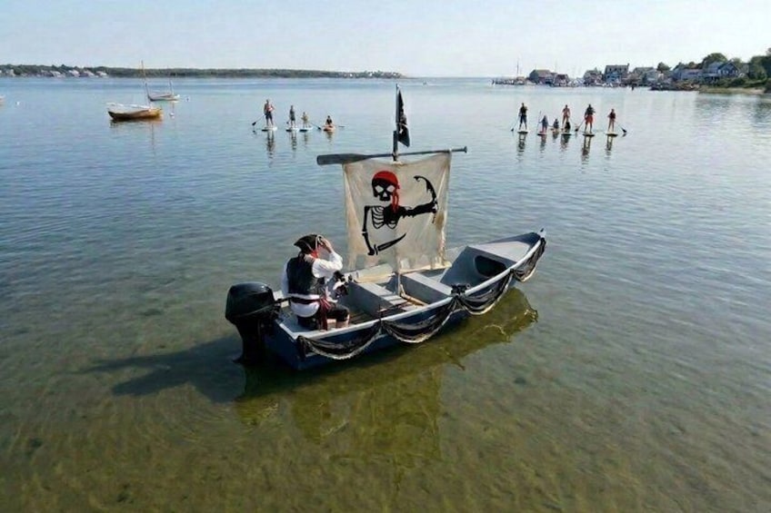 A small boat with a skeleton flag, people in the water, and a calm lake. 2