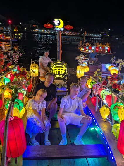 A group of people sitting on a boat decorated with colorful lanterns and flowers, with a night scene in the background. 2