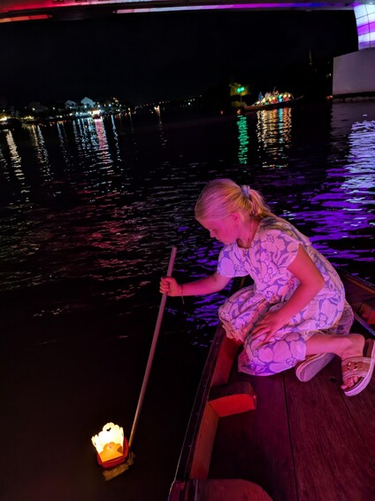 A person in a boat at night, holding a pole, with a lit lantern on the water. 5