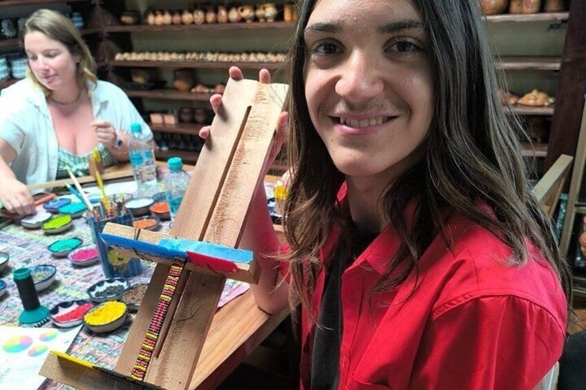 Una persona sostiene una tabla de madera con pinceles y recipientes de pintura sobre una mesa. 4