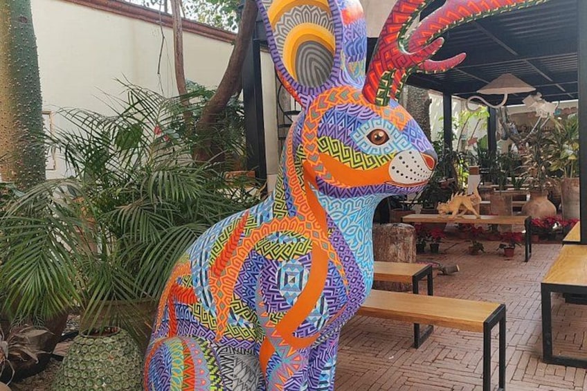 Une sculpture colorée et richement décorée représentant un lapin, placée dans un espace extérieur agrémenté de plantes en pot et de bancs en bois. 3