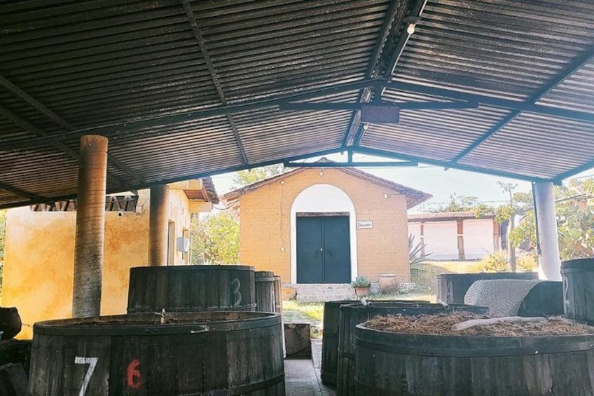 Un espace extérieur abrité, doté de grands conteneurs cylindriques, un bâtiment en briques avec une porte et une structure de toit en métal. 2