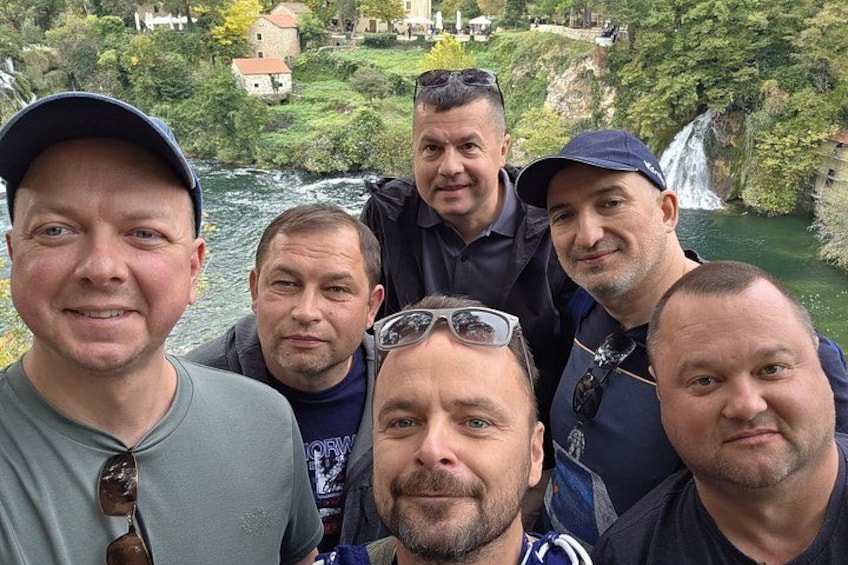 En gruppe mennesker står ved en flod med et vandfald i baggrunden. 3