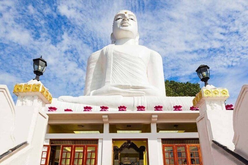 A large white statue of a seated figure, surrounded by a white building with red-framed windows and yellow decorative elements. 3