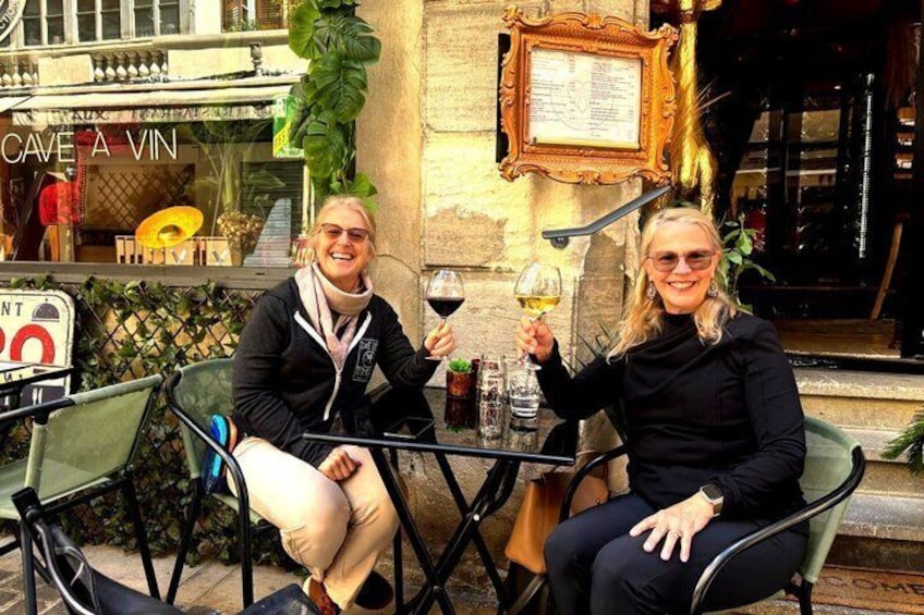 Two people sitting at a table outside a cafe with a menu board above them. 1